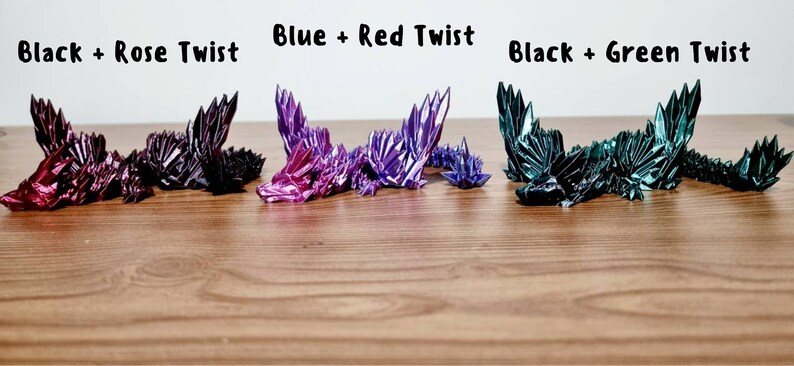 Peut inclure: Quatre dragons en origami dans diff&eacute;rentes combinaisons de couleurs&nbsp;: noir et rose, bleu et rouge, noir et vert. Les dragons sont couch&eacute;s sur une surface en bois.