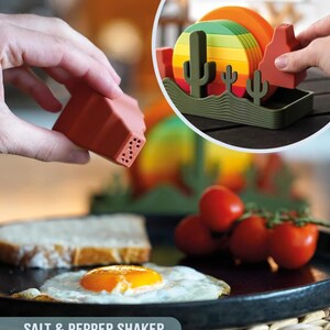 May include: A terracotta-colored salt and pepper shaker set with a desert landscape design. The set includes a salt shaker, pepper shaker, and a holder with cacti and a mesa. The text "SALT & PEPPER SHAKER" is at the bottom.