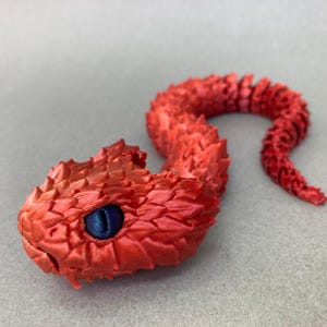 May include: A red 3D printed snake with a blue eye. The snake is curled up in a coil shape.