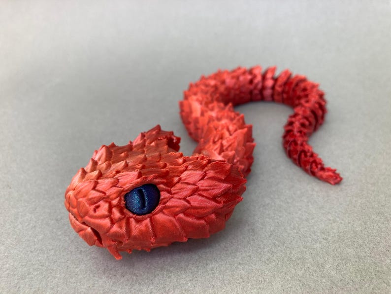 May include: A red 3D printed snake with a blue eye. The snake is curled up in a coil shape.
