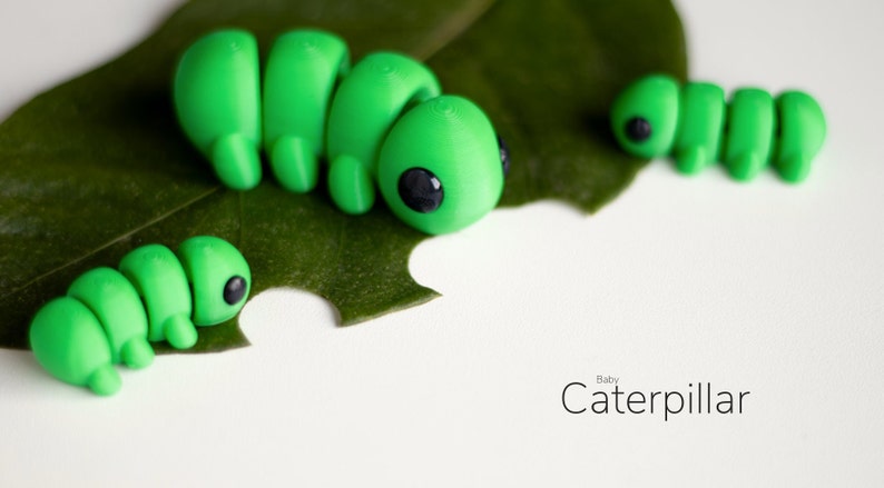 Puede incluir: Primer plano de varias figuras de orugas verde brillante con ojos negros, posadas sobre una hoja verde con una mordida. El texto "Baby Caterpillar" est&aacute; escrito en una fuente delicada en la parte inferior derecha.