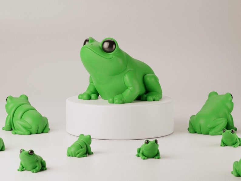 May include: A collection of green frog figurines. One large frog sits atop a white pedestal, surrounded by smaller frog figures. The frogs have large, black eyes and a glossy finish, creating a playful and whimsical aesthetic.
