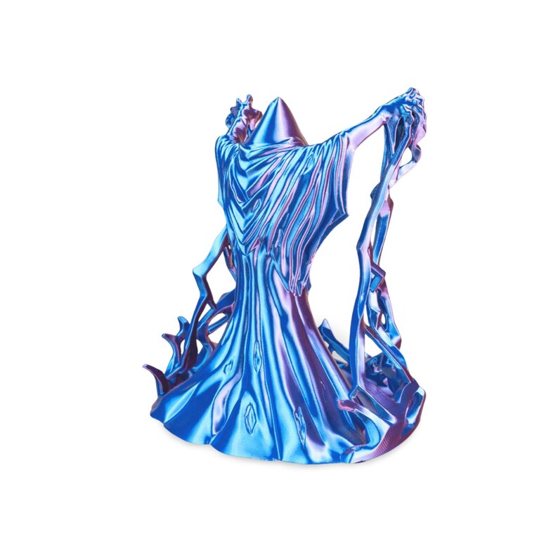 Puede incluir: Una escultura iridiscente azul y p&uacute;rpura de una figura con t&uacute;nica y los brazos extendidos. La figura tiene un sombrero puntiagudo y t&uacute;nicas fluidas, con elementos dentados en forma de rayo que se extienden desde la base y los brazos.