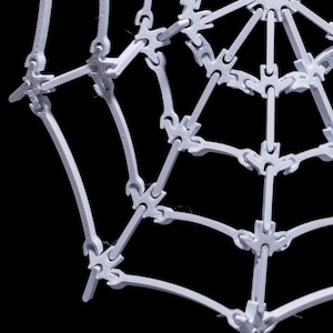 May include: A white plastic spider web decoration with a circular center and radiating spokes. The web is made of interlocking pieces that create a three-dimensional effect.