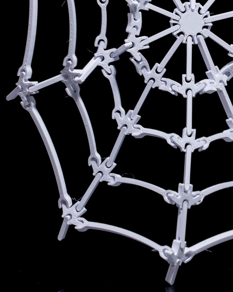 May include: A white plastic spider web decoration with a circular center and radiating spokes. The web is made of interlocking pieces that create a three-dimensional effect.