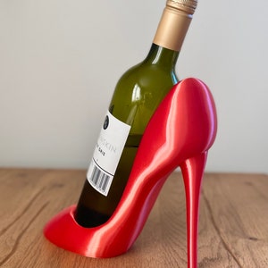 May include: A red high heel shoe shaped wine bottle holder. A bottle of white wine is in the holder.