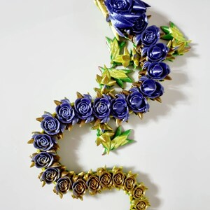 Peut inclure: Une guirlande florale violette et dor&eacute;e faite de roses et de feuilles en tissu. La guirlande est en forme de serpent ou de dragon.
