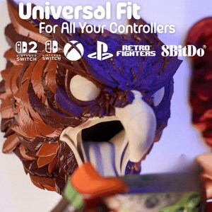 May include: A detailed, multi-colored owl-shaped controller holder. The text "Universal Fit For All Your Controllers" is displayed above the owl. Logos for Nintendo Switch, Xbox, Playstation, Retro Fighters, and 8BitDo are also visible.