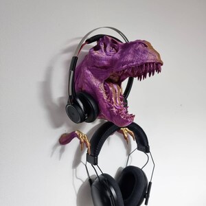 May include: A purple and gold dinosaur head sculpture with a pair of black headphones hanging from its mouth.