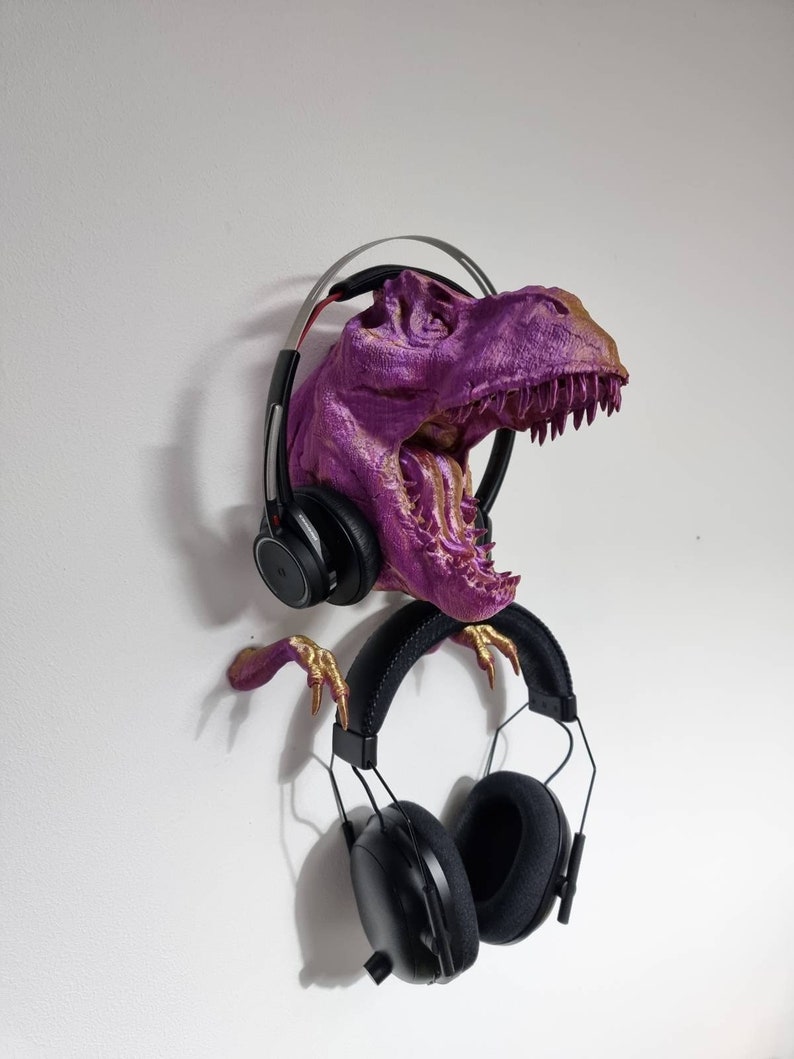 May include: A purple and gold dinosaur head sculpture with a pair of black headphones hanging from its mouth.