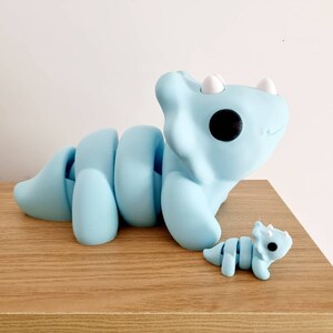 Puede incluir: Dos juguetes de dinosaurio de pl&aacute;stico azul claro. El dinosaurio m&aacute;s grande es un triceratops con la cola enroscada. El dinosaurio m&aacute;s peque&ntilde;o es un triceratops con la cola recta.