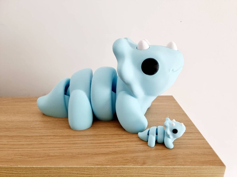 Puede incluir: Dos juguetes de dinosaurio de pl&aacute;stico azul claro. El dinosaurio m&aacute;s grande es un triceratops con la cola enroscada. El dinosaurio m&aacute;s peque&ntilde;o es un triceratops con la cola recta.