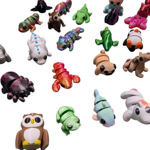 Peut inclure: Une collection de figurines d'animaux miniatures color&eacute;es. L'assortiment comprend une araign&eacute;e, un homard, un hibou, une grenouille et d'autres cr&eacute;atures de diff&eacute;rentes couleurs et finitions. Les figurines sont dispos&eacute;es sur un fond blanc.