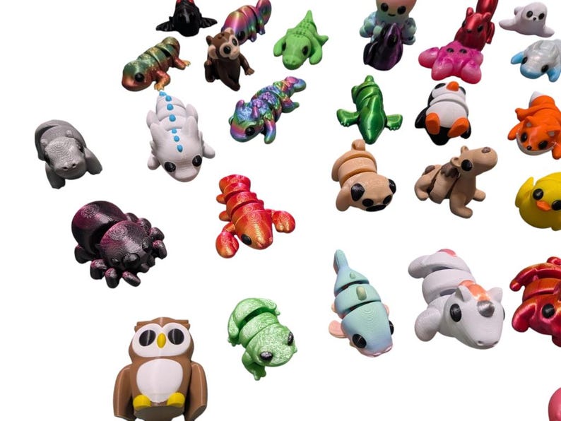 Peut inclure: Une collection de figurines d'animaux miniatures color&eacute;es. L'assortiment comprend une araign&eacute;e, un homard, un hibou, une grenouille et d'autres cr&eacute;atures de diff&eacute;rentes couleurs et finitions. Les figurines sont dispos&eacute;es sur un fond blanc.