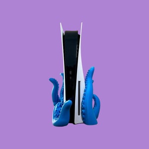 May include: A white and black video game console with a blue octopus-shaped stand. The console is standing upright and the stand is holding it in place.