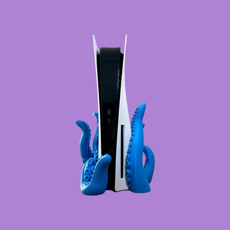May include: A white and black video game console with a blue octopus-shaped stand. The console is standing upright and the stand is holding it in place.