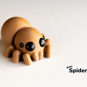May include: A brown, 3D printed, cartoon spider with large black eyes. The spider is sitting on a white surface. The text "Baby Spider" is written below the spider.