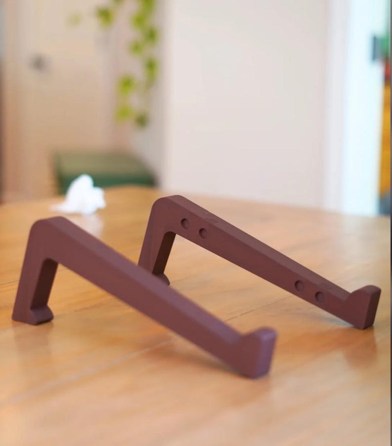 Peut inclure: Deux supports pour ordinateur portable bruns sont inclin&eacute;s sur une surface en bois. Chaque support a une base rectangulaire et un support inclin&eacute; avec trois petits trous. Les supports sont con&ccedil;us pour sur&eacute;lever un ordinateur portable.