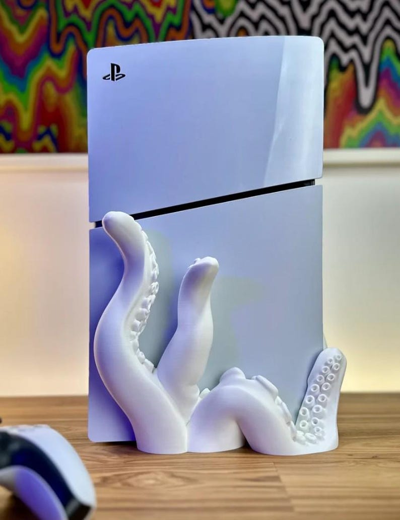 May include: A white PlayStation 5 console with a 3D printed white octopus stand. The octopus tentacles wrap around the console and have suction cups.