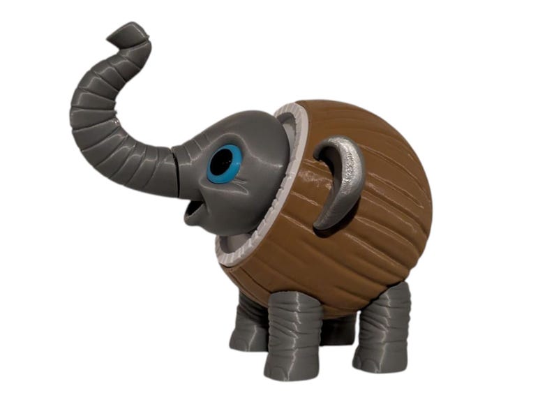 May include: A whimsical 3D-printed elephant figurine. The elephant has a gray head, trunk, and legs, with blue eyes and a brown, textured body. The trunk is curved upwards, and the ears are silver.