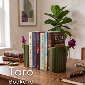 May include: Olive green bookends with a vertical ribbed design, holding a collection of books. The bookends have small vases for flowers. The text "Taro Bookend" is at the bottom. Books include "Dune" and "To Kill a Mockingbird".