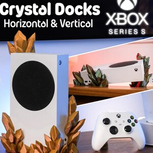 May include: White Xbox Series S console with a black circular vent and a matching white controller. The console is displayed with decorative crystal-shaped accents in shades of gold and green. The text "Crystal Docks Horizontal & Vertical" is visible.