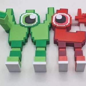 May include: Two pixelated figures, one green and one red, stand side-by-side. The green figure has an arm raised, while the red figure points a finger. Both have large, round eyes and blocky features, reminiscent of retro video game characters.