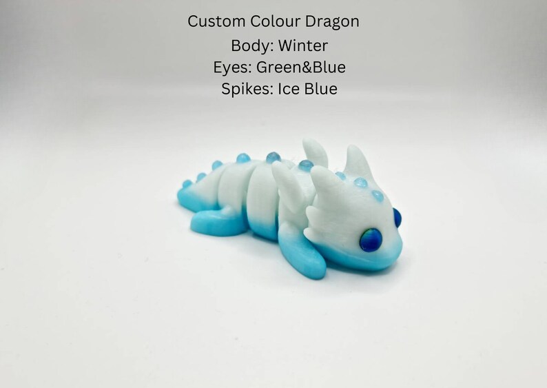 May include: A small, white and blue dragon figurine with green and blue eyes. The dragon has a winter white body with blue accents and ice blue spikes.
