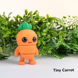May include: A small, orange carrot-shaped figurine with a green leafy top and a smiling face. The figurine is made of clay and has a cartoonish appearance. The figurine is sitting on a white surface with green foliage in the background. The text "Tiny Carrot" is written below the figurine.