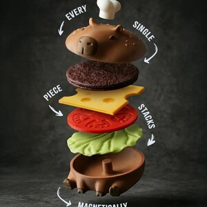 Op de afbeelding: Een grillige, gedemonteerde burgerset met een capibara-vormig broodje, een koksmuts en burgerlagen. De tekst luidt: "Elk stuk stapelt magnetisch."