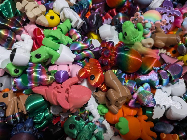 Peut inclure: Un ensemble de jouets imprim&eacute;s en 3D aux couleurs vives, dont des grenouilles, des astronautes et des formes abstraites. Les jouets sont de diff&eacute;rentes couleurs, notamment vert, orange, rose et arc-en-ciel. Gros plan des jouets.