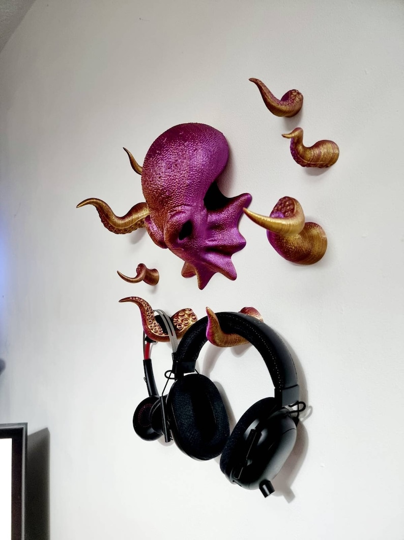May include: A purple and gold octopus wall mount with eight tentacles, used to hang headphones. The octopus is 3D printed and has a textured surface.