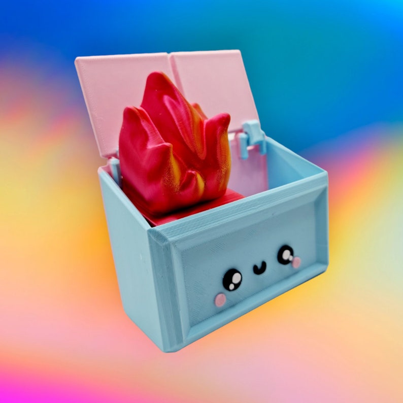 May include: A light blue box with a pink lid and a red and yellow flame inside. The box has a cute cartoon face with black eyes and pink cheeks.