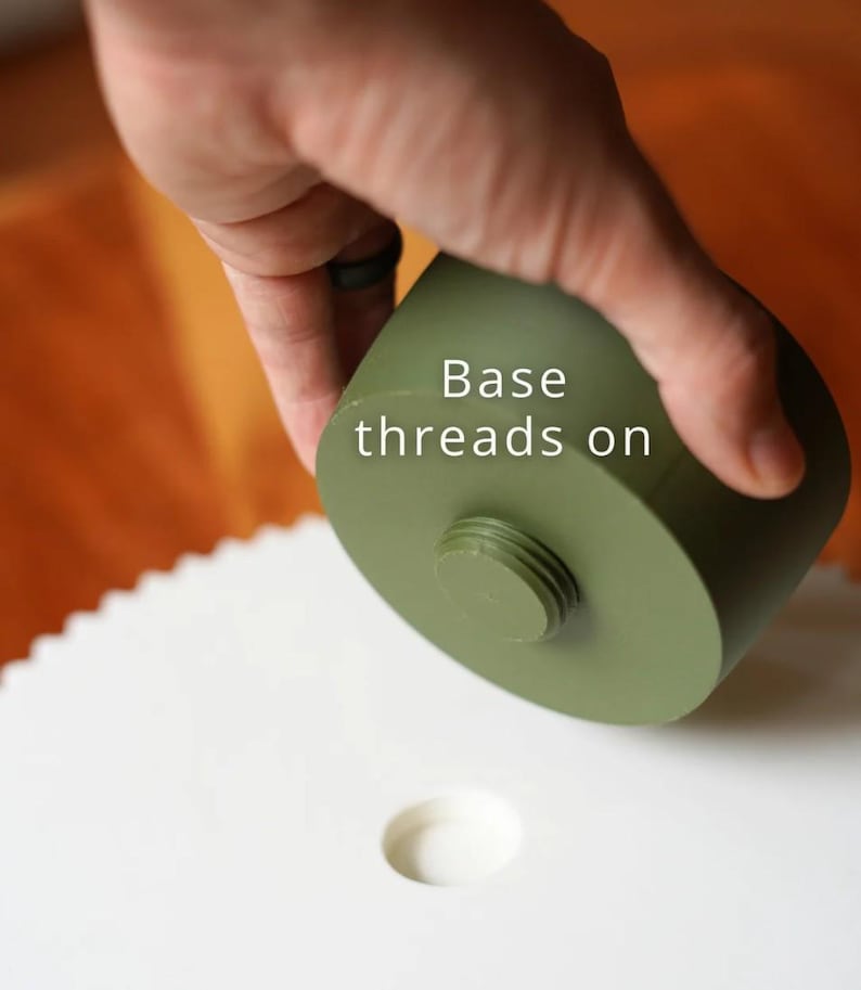 Puede incluir: Un objeto cil&iacute;ndrico verde oliva con una base roscada, colocado sobre una superficie blanca con un agujero circular. El texto "Base threads on" es visible. La imagen se centra en el dise&ntilde;o del objeto.