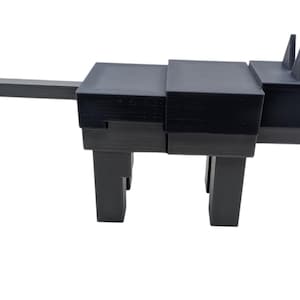 May include: A black, geometric sculpture of an animal, possibly a cat or dog, with a long tail and upright ears. The sculpture is constructed from stacked rectangular blocks and stands on four legs. The design is modern and minimalist.