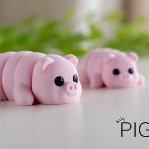 Puede incluir: Dos figuras de cerdos rosas con ojos negros y orejas peque&ntilde;as se exhiben sobre una superficie blanca. Las figuras de cerdos est&aacute;n en posici&oacute;n de gateo. El texto "baby PIG" est&aacute; escrito en negro en el lado derecho de la imagen.