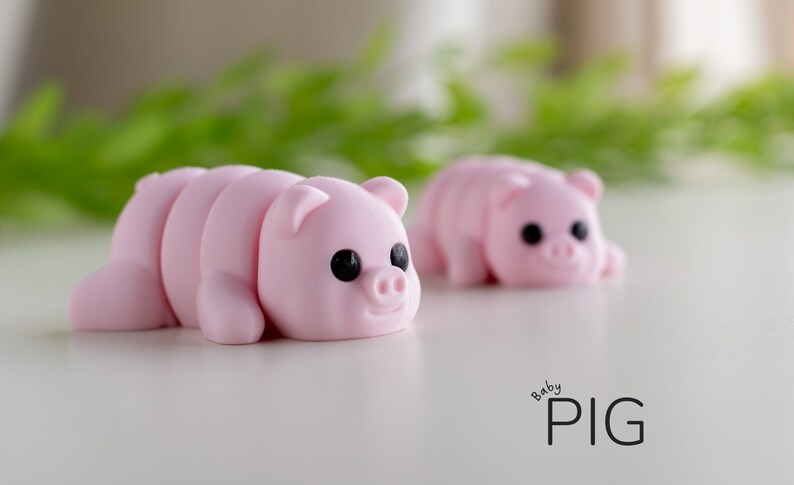 Puede incluir: Dos figuras de cerdos rosas con ojos negros y orejas peque&ntilde;as se exhiben sobre una superficie blanca. Las figuras de cerdos est&aacute;n en posici&oacute;n de gateo. El texto "baby PIG" est&aacute; escrito en negro en el lado derecho de la imagen.