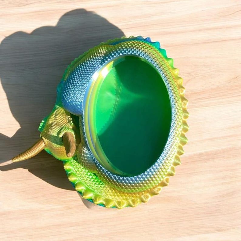 May include: A green, blue, and gold iridescent dinosaur-shaped trinket dish with a round, hollow center.