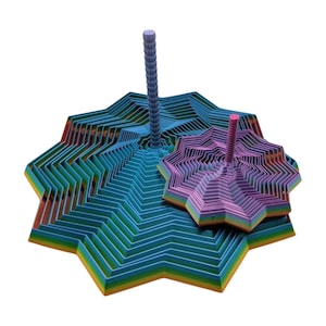 Puede incluir: Una escultura geométrica colorida y en capas con una base grande y multicolor y un pilar central texturizado. Una escultura más pequeña y similar se encuentra al lado. La base presenta tonos de azul, verde, naranja y amarillo.