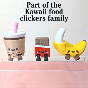 May include: Three Kawaii food clickers: a boba tea with a pink straw, a chocolate bar in red packaging, and a yellow banana. Each has a smiling face and small legs. Text reads "Part of the Kawaii food clickers family."