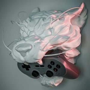 May include: A white, sculpted cat head with a gray video game controller. The cat head has a textured, cloud-like appearance. The controller has black buttons and a directional pad. The overall aesthetic is modern and artistic.