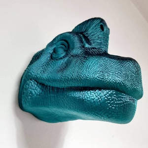 May include: Teal blue dinosaur head sculpture with a textured surface. The dinosaur's mouth is slightly open, and its eye is visible.