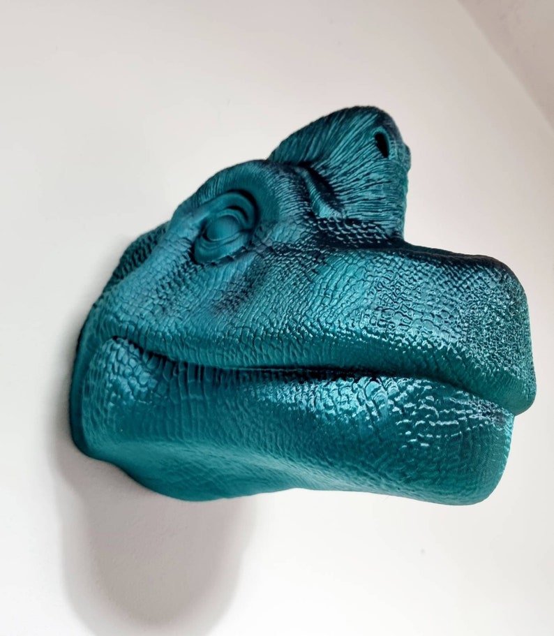 May include: Teal blue dinosaur head sculpture with a textured surface. The dinosaur's mouth is slightly open, and its eye is visible.