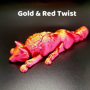 May include: A red and gold metallic wolf figurine with a textured fur design. The wolf is lying down with its head turned to the side. The figurine is made of plastic and is approximately 6 inches long.