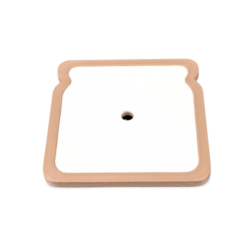 May include: A square, white cutting board with a tan, bread-shaped border. The cutting board has a small, black hole in the center. The board is on a white background.