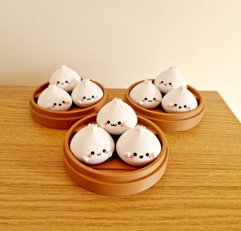 May include: Eight white ceramic dumplings with cute faces are arranged in three brown bamboo steamer baskets. The dumplings are all the same size and shape, and they have small pink cheeks and black eyes.