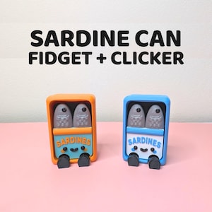 Op de afbeelding: Twee novelty fidget clickers in de vorm van sardineblikjes. Eén is oranje en blauw, de andere blauw en oranje. Elk heeft een lachend gezicht en het woord "Sardines". De tekst bovenaan luidt "Sardine Can Fidget + Clicker".