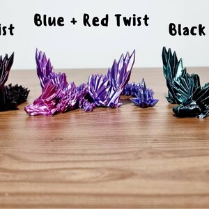 May include: Four origami dragons in different color combinations: black and rose, blue and red, black and green. The dragons are lying on a wooden surface.
