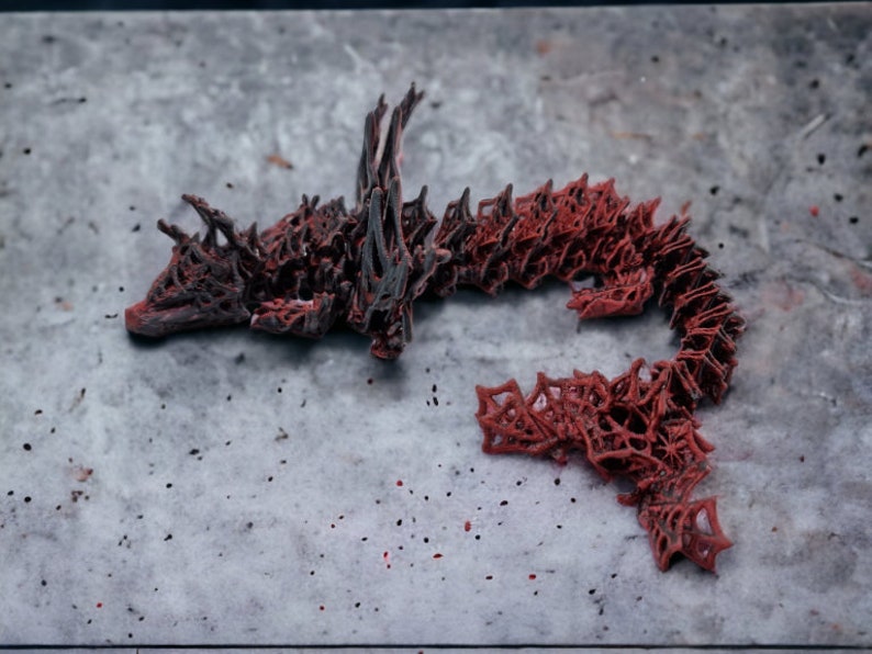 May include: An abstract sculpture resembling a dragon or serpent, predominantly red with dark grey detailing. The intricate, openwork design is set against a mottled grey surface. The artwork is a unique, decorative piece.