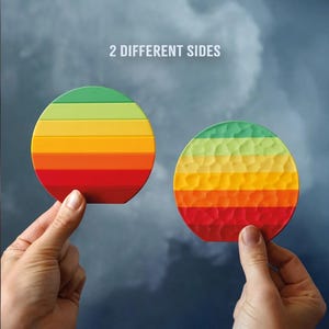 May include: Two round coasters with a gradient of colors from red to green. One coaster has a smooth surface, and the other has a textured surface. The text "2 DIFFERENT SIDES" is above the coasters.